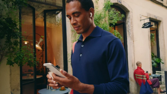 Un hombre con AirPods mira su iPhone en una calle